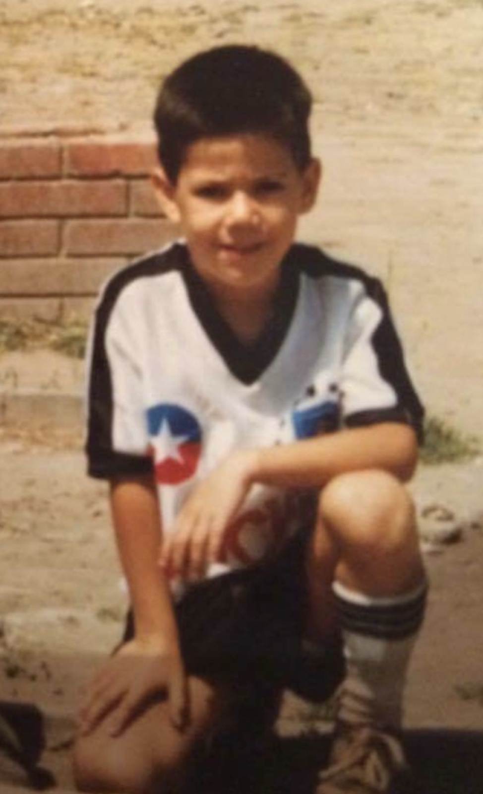 Chris aged five in a Chile national football shirt, crouched against a brick wall in Chile